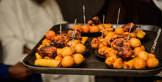 Server presenting assorted Nigerian small chops platter, featuring puff-puff, grilled chicken, samosas, and spring rolls at a social event in Lagos